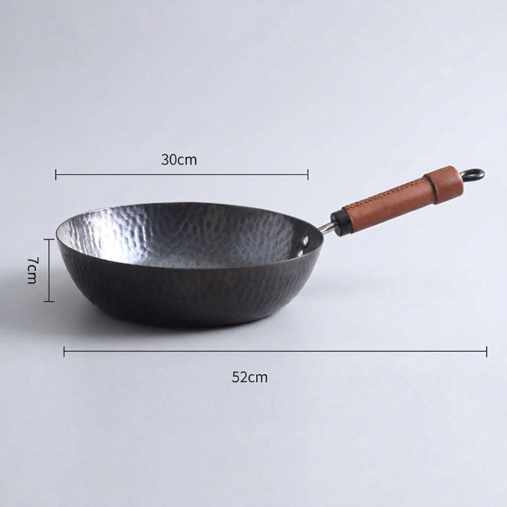 A hammered metal wok with a brown leather-wrapped handle, shown on a light gray background with overlaid dimension lines and text indicating 28 cm width, 7 cm depth, and 50 cm total length.