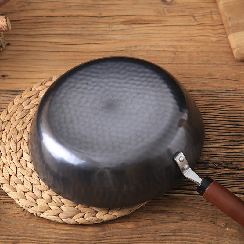 Black frying pan with a textured surface on a wooden table