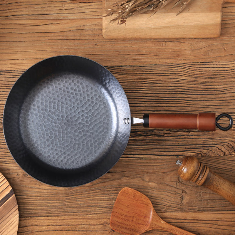 Black frying pan with a textured surface on a wooden table with kitchen utensils.