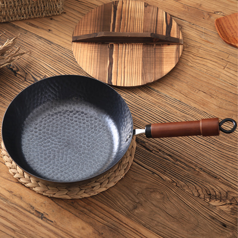 Black frying pan with a brown handle on a wooden surface