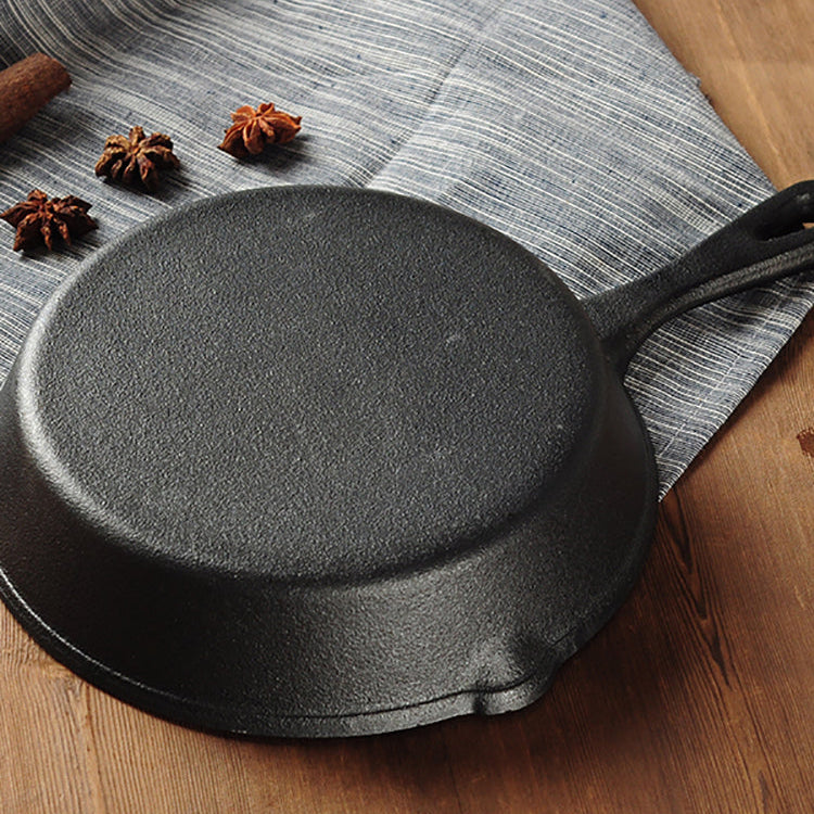 Black cast iron skillet on a wooden surface with a gray cloth underneath