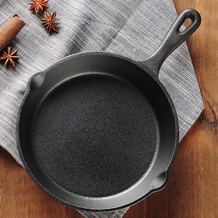 Black cast iron skillet on a wooden surface with a gray cloth underneath