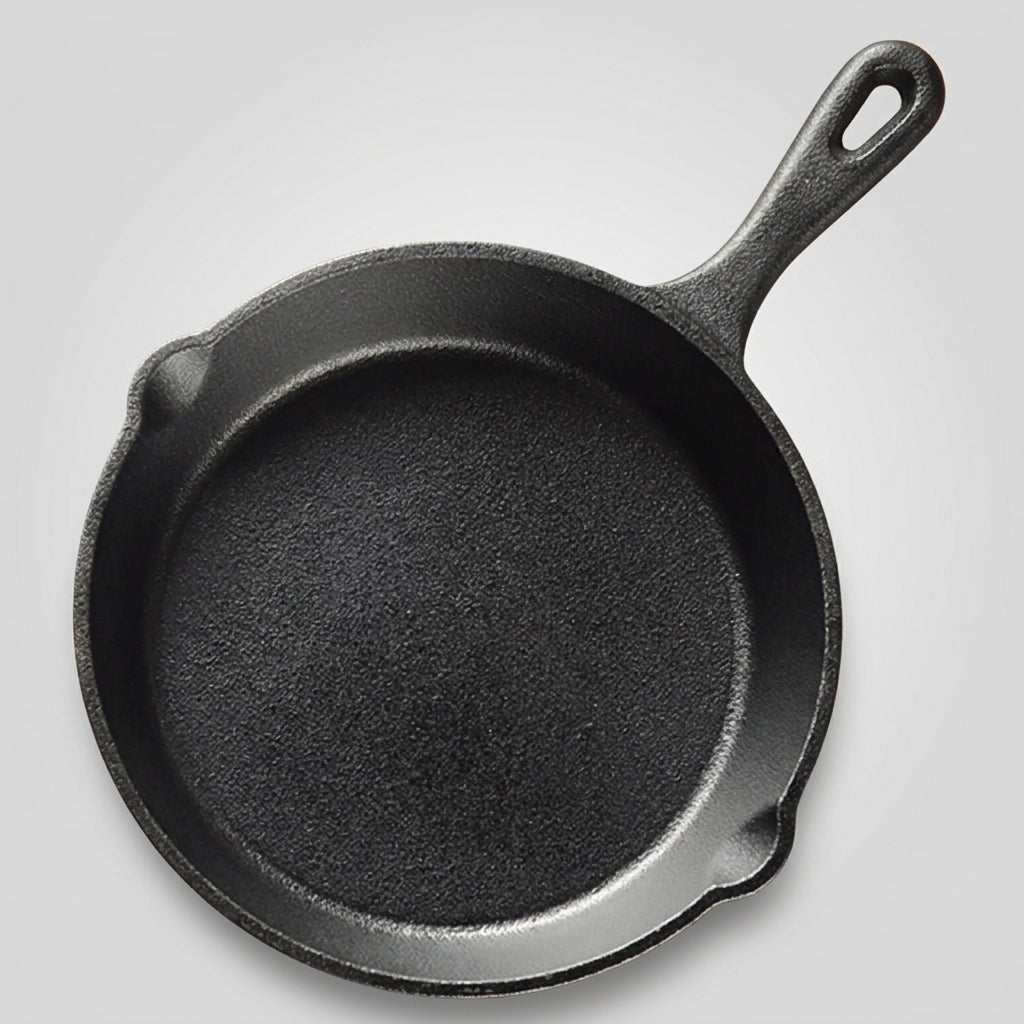 A black cast iron skillet with a long handle, photographed from above on a gray striped cloth over a wooden surface, with cinnamon sticks and star anise nearby.